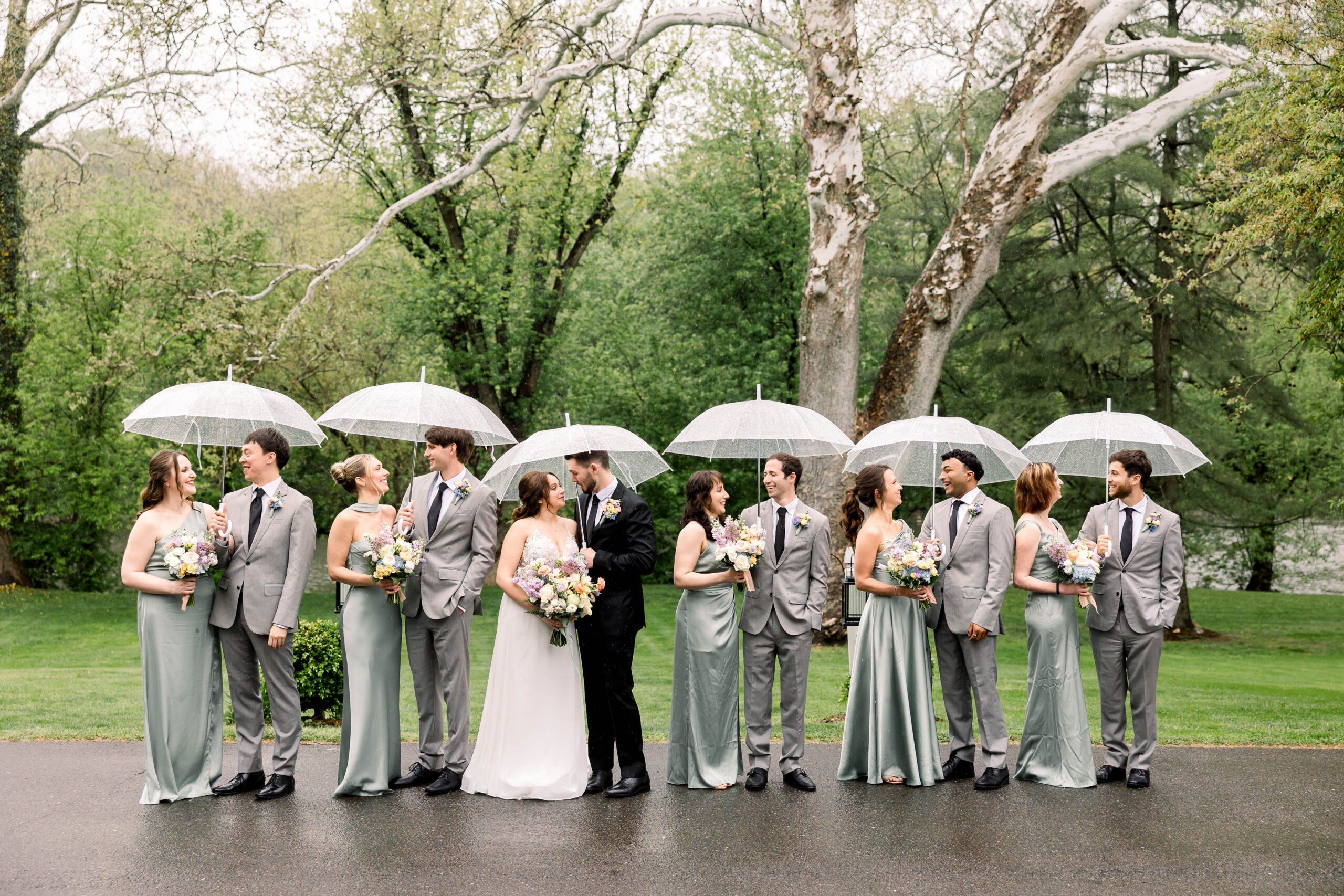 A couple and their wedding party under clear umbrellas on their rainy wedding day at Riverdale Manor
